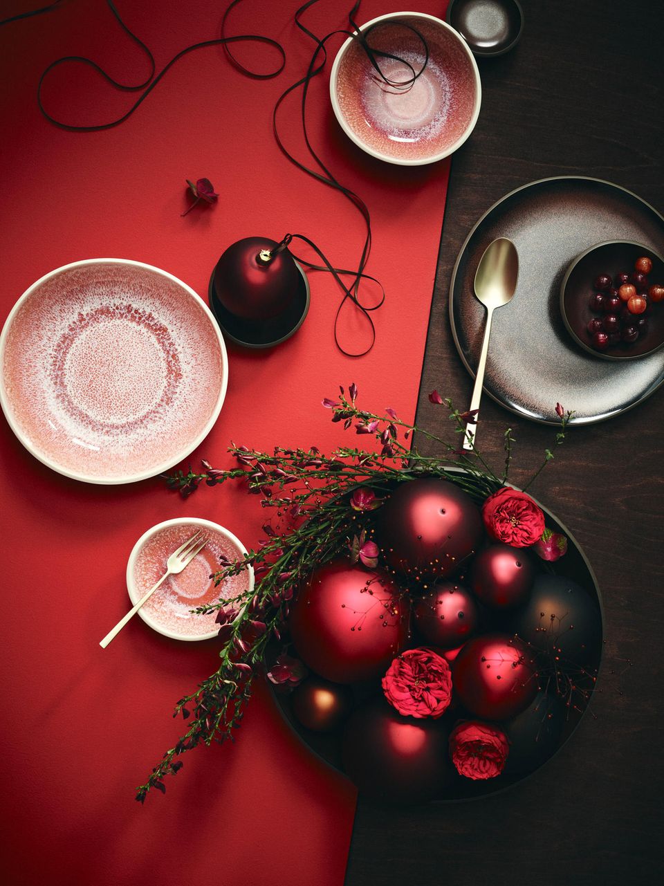Rosa gesprenkeltes Geschirr auf rubinrotem Tischläufer mit Gesteck aus granatapfelfarbenen Weihnachtskugeln
