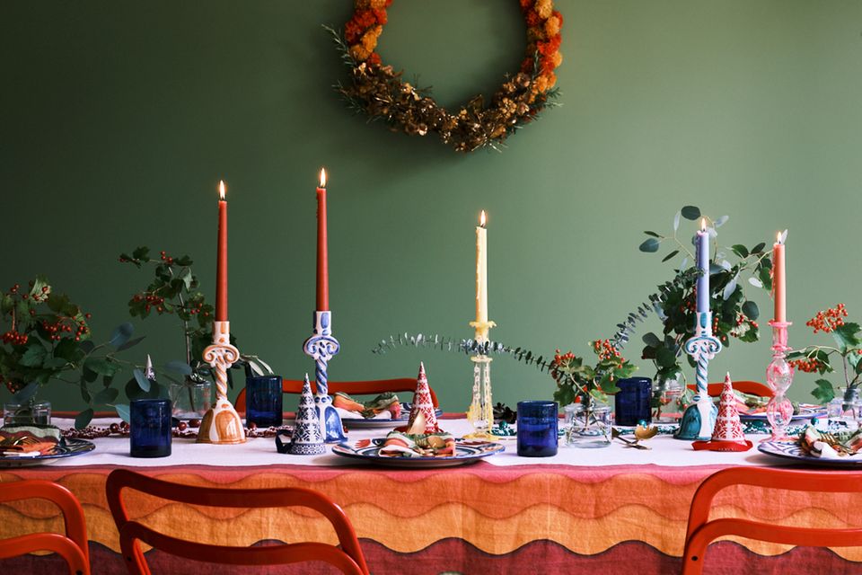 Bunt gedeckter Tisch in allen Regenbogenfarben mit Pompomkranz an grüner Wand und weihnachtlichen Sträußen mit Eukalyptus