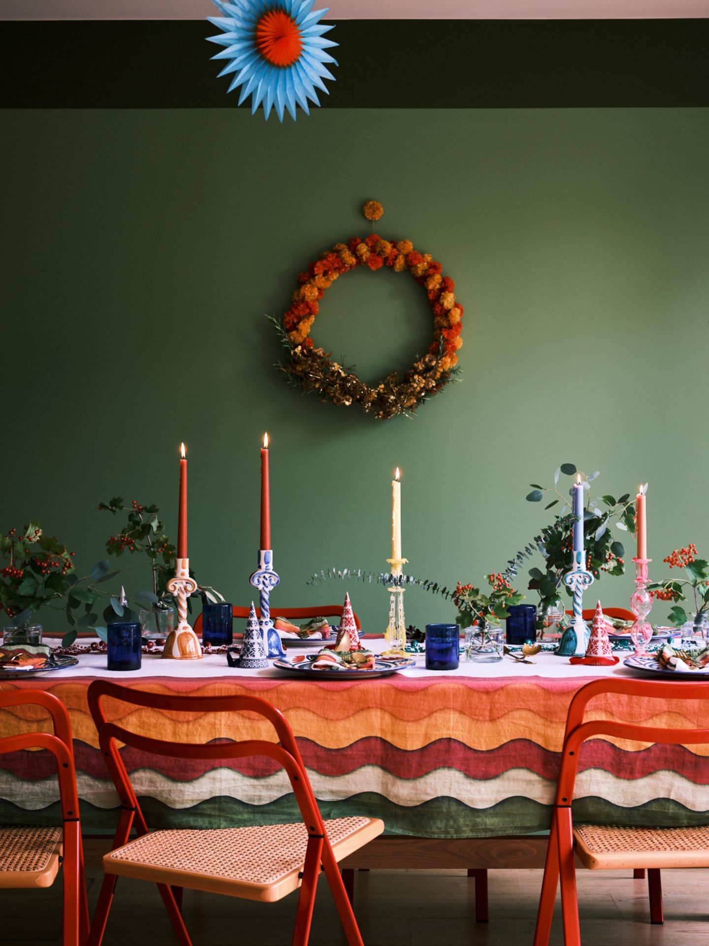 Bunt gedeckter Tisch in allen Regenbogenfarben mit Pompomkranz an grüner Wand und weihnachtlichen Sträußen mit Eukalyptus