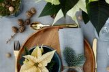 Tischdeko mit Holztellern, goldenem Besteck und cremeweißen Weihnachtssternen als Gastgeschenk
