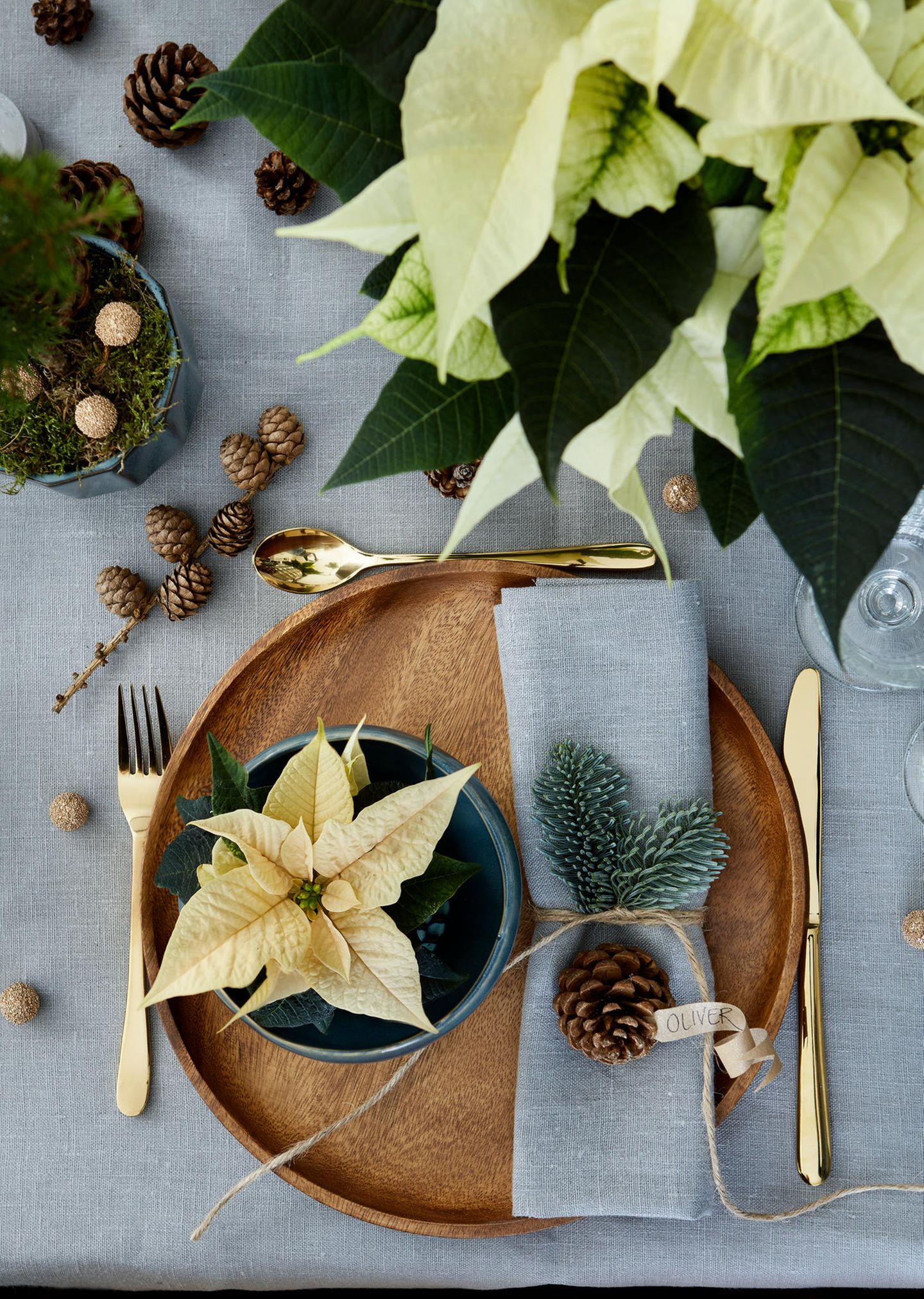 Tischdeko mit Holztellern, goldenem Besteck und cremeweißen Weihnachtssternen als Gastgeschenk