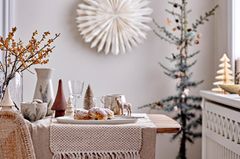 Winterlich dekorierter Tisch im Wohnzimmer in Erdtönen mit Papierstern an der Wand und skandinavischem Weihnachtsbaum