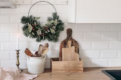 Weihnachtlich dekorierter Metallring mit Tannenzweigen und Eukalyptus in einer weißen Küche mit Accessoires und Holzbrettchen