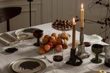 Puristische Tischdeko mit grau-schwarzen Tellern, Kerzenhaltern in rustikalen Farben und einer weißen bestickten Decke