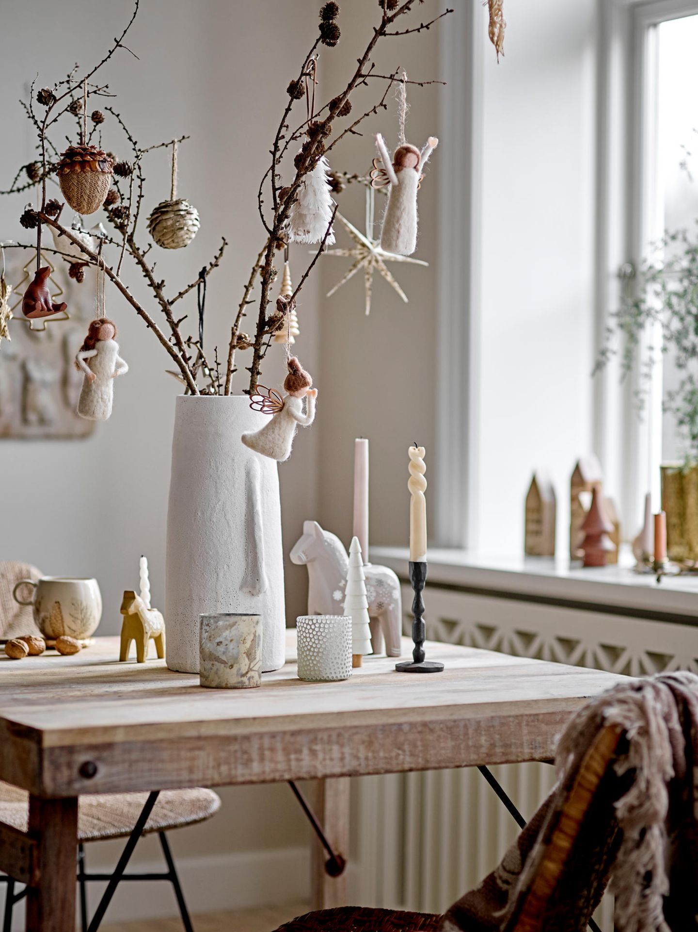 Tischdeko aus weißer Vase mit Zweigen, Zapfen, Filzengeln und Dalapferden als Kerzenhaltern