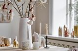 Tischdeko aus weißer Vase mit Zweigen, Zapfen, Filzengeln und Dalapferden als Kerzenhaltern
