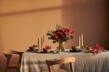 Tischdeko in Apricot und Beigetönen mit Kerzenhaltern, rustikaler Tischdecke und rot-apricotfarbenem Blumenstrauß