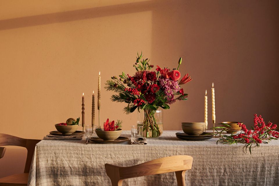 Weihnachtlich dekorierter Tisch mit einem Blumenstrauß, karieter Tischdecke und einer Wand in Ocker
