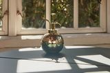 Eine goldene Sprühflasche für Pflanzen steht vor auf einer Fensterbank eines Strebenfensters
