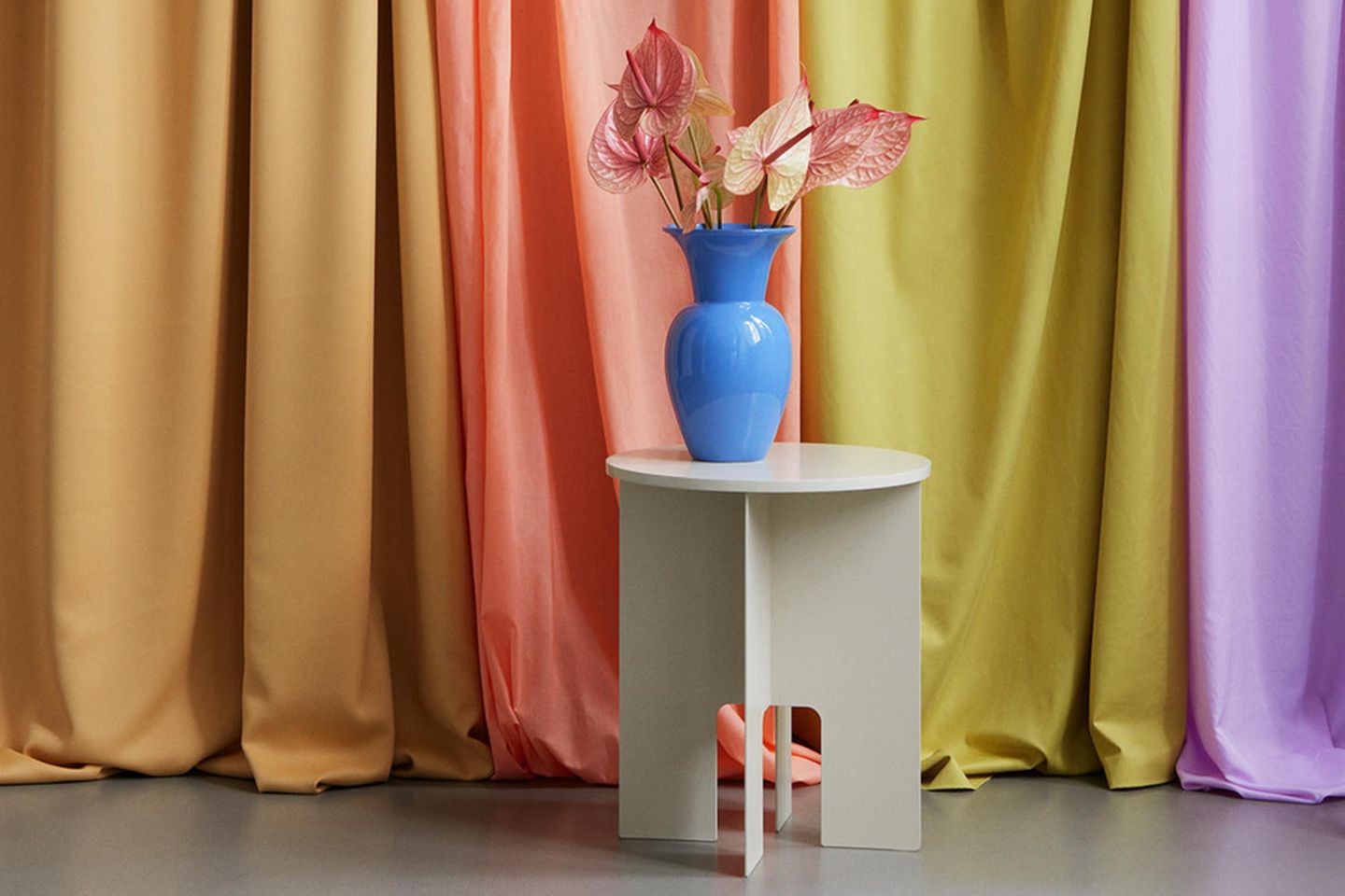 Blaue Vase auf beigefarbenem Beistelltisch vor bunten Vorhängen