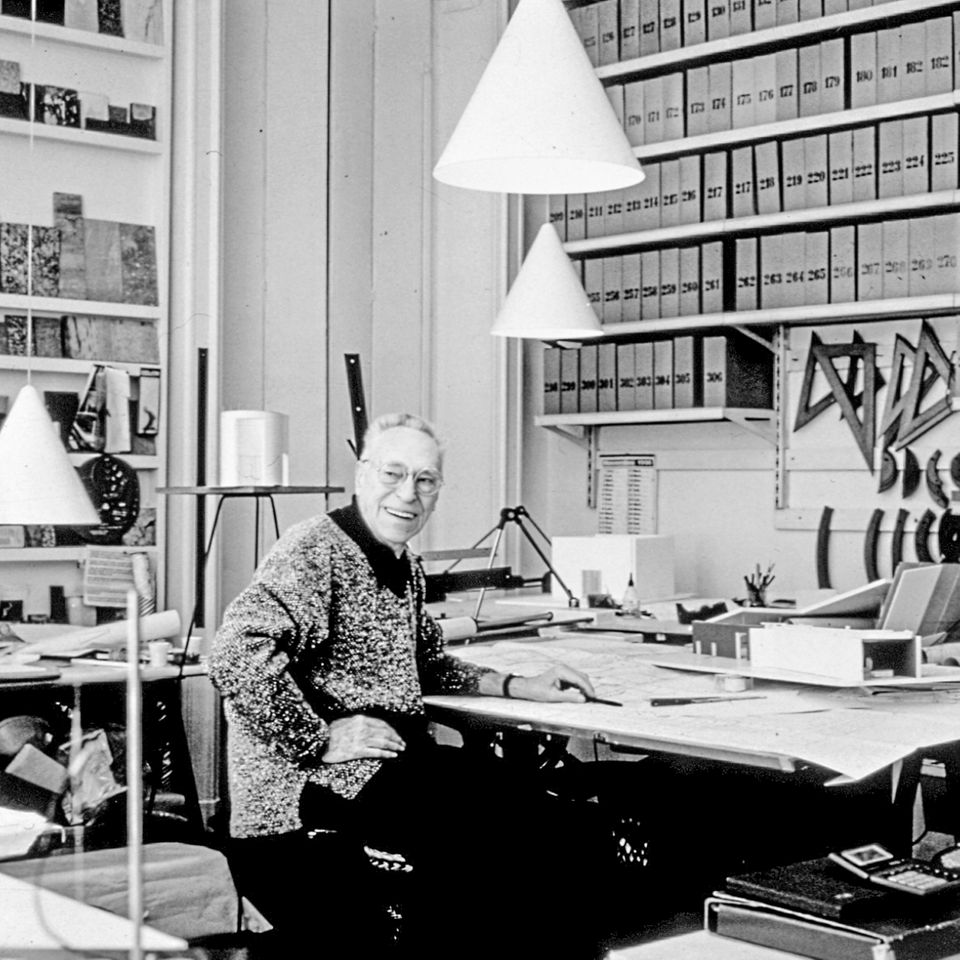 Achille Castiglioni (1918–2002) gestaltete Leuchten, Möbel und Gebrauchsgegenstände und war eine der prägendsten Figuren der italienischen Nachkriegsmoderne. Gemeinsam mit seinem früh verstorbenen Bruder Pier Giacomo Castiglioni (1913–1968) entstanden die Objekte der Readymade-Serie, zu denen auch die Leuchte "Toio" gehört.