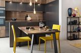 Dunkle Küche in Holzoptik aus Lacklaminat mit gelben Stühlen am Esstisch