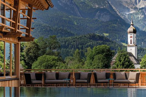 Hotelpool neben einem Hozhaus vor einer Alpenkulisse mit einem Kirchturm
