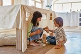Spielende Kinder unter Tisch mit Tischdecke in Form eines Spielhauses