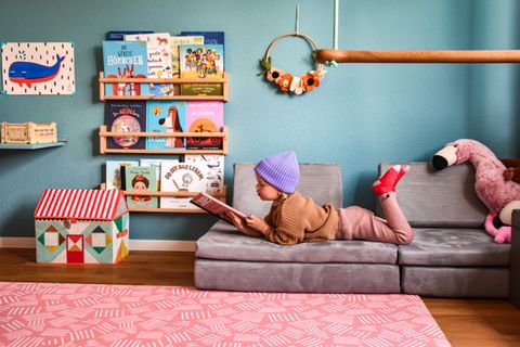Kind lesend auf grauem Spielsofa in buntem Kinderzimmer