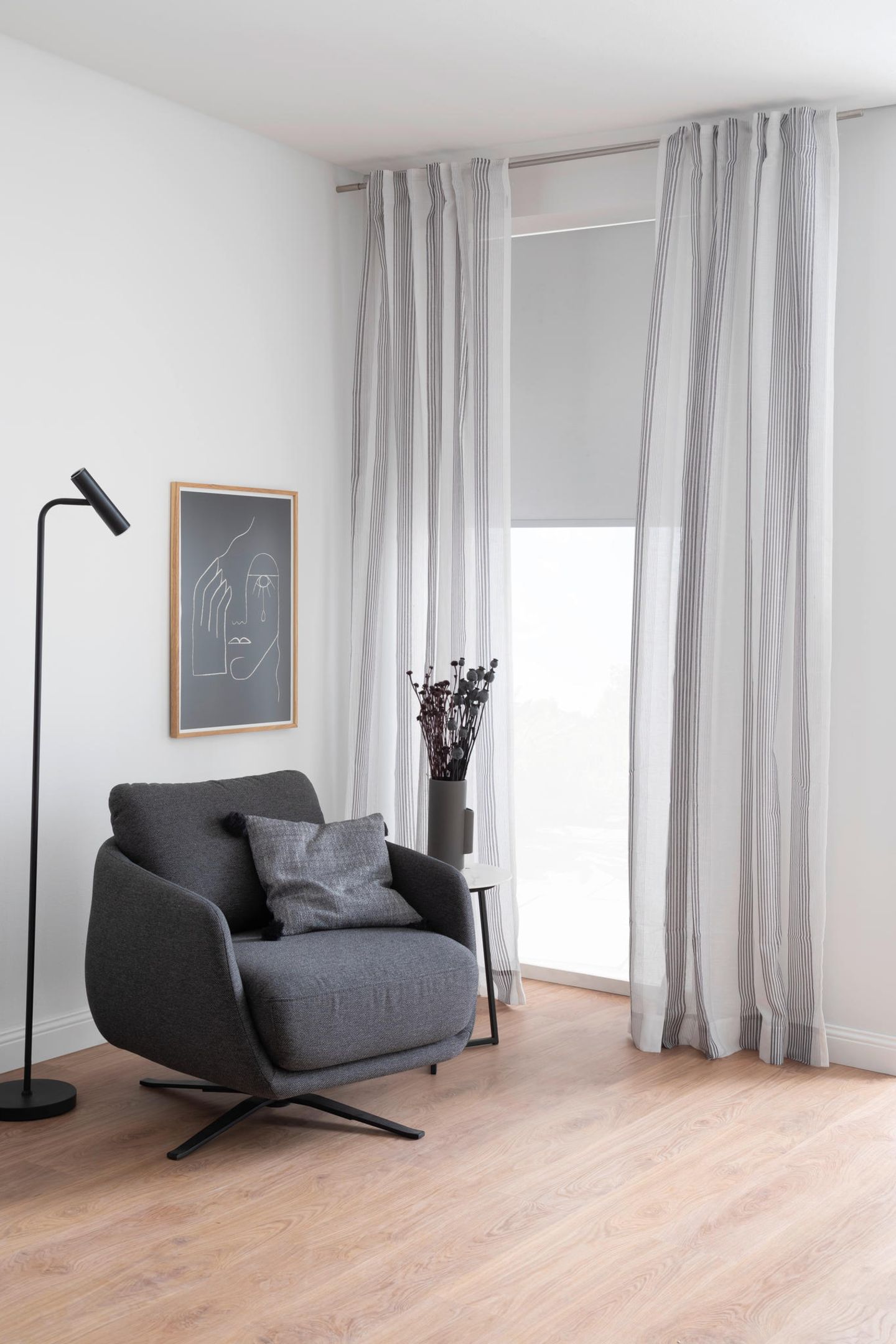 Grauer Sessel vor Fenster mit langen, grauen Vorhängen