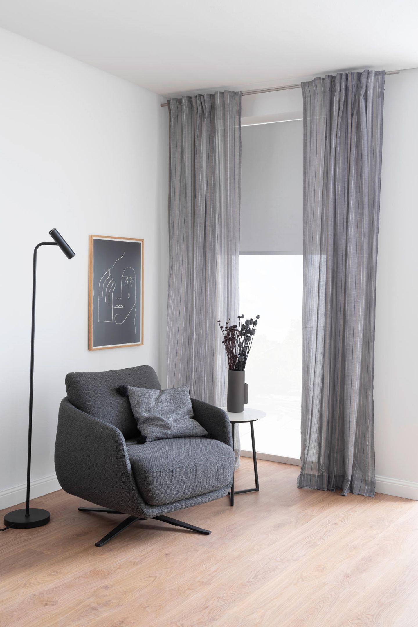 Grauer Sessel vor Fenster mit langen, weißen Vorhängen