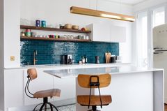 Betonleuchte von Gant Lights über einer weißen Kücheninsel mit petrolfarbenem Fliesenspiegel und Holzstühlen