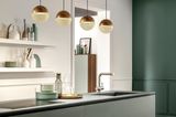 Goldene Pendelleuchten über einem Küchentresen einer Küche in Grau, Dunkelgrün und Weiß