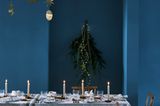 Dunkelblau gestrichenes Esszimmer mit weiß und rustikal eingedecktem Tisch, Kerzen und goldenem Mobilé