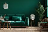 Dunkelgrün gestrichenes Wohnzimmer mit samtgrünem Sofa und dunklen Holzmöbeln sowie hellen Glasleuchten