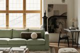 Salbeigrünes Sofa vor hoher Glasfront in einem Loft-Wohnzimmer mit weißem Teppich und großem Wohnzimmertisch