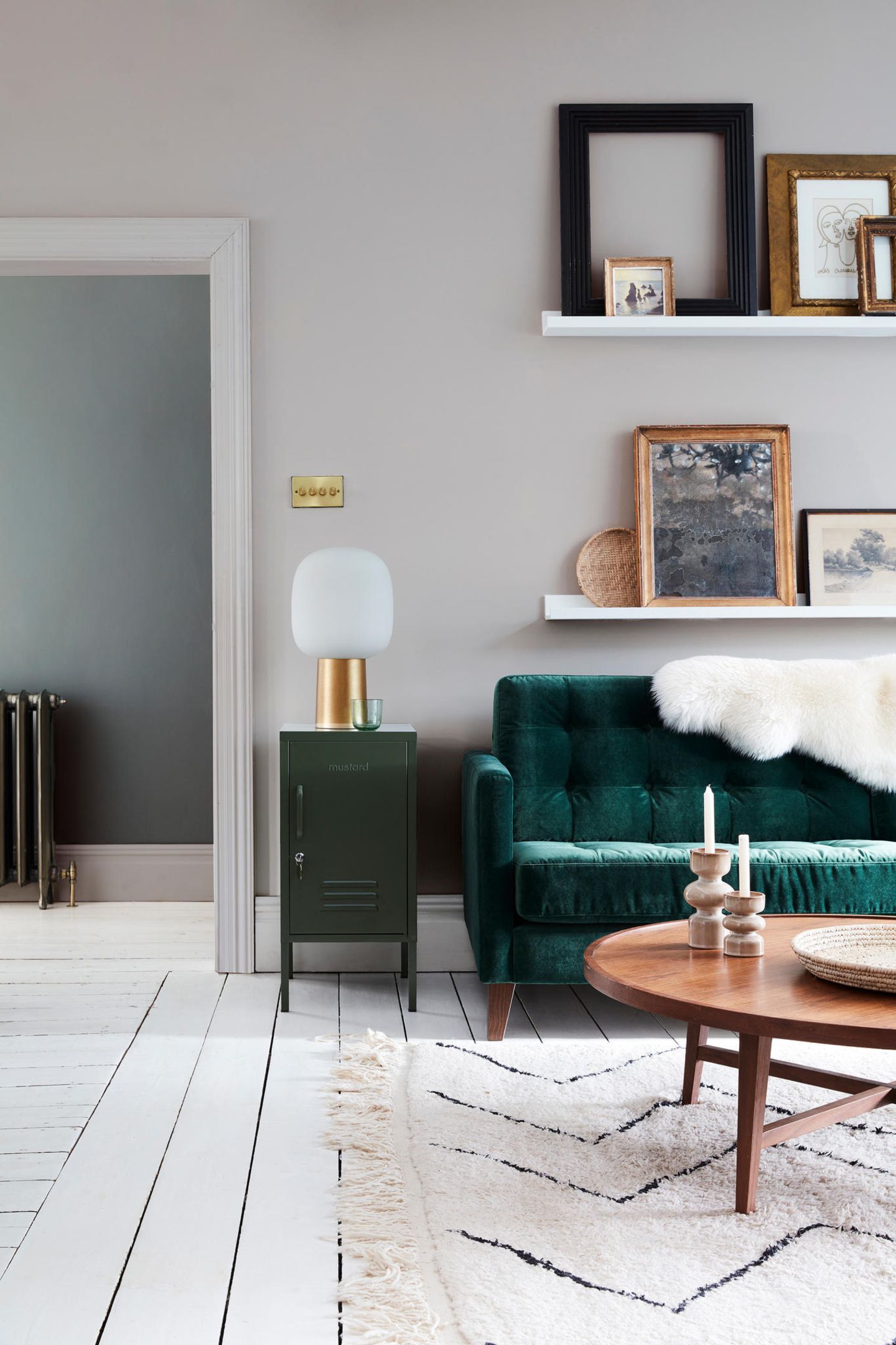 Samtgrünes Sofa in grau gestrichenem Wohnzimmer mit Schafsfell und Bilderleisten sowie Midcentury-Holztisch