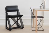 Gestapelte schwarze Stühle aus schwarzem Draht, ein Stuhl aufgeklappt stehend an Holztisch