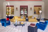 Gelbes Modulsofa und blaue Sessel in Wohnzimmer mit kariertem Teppich