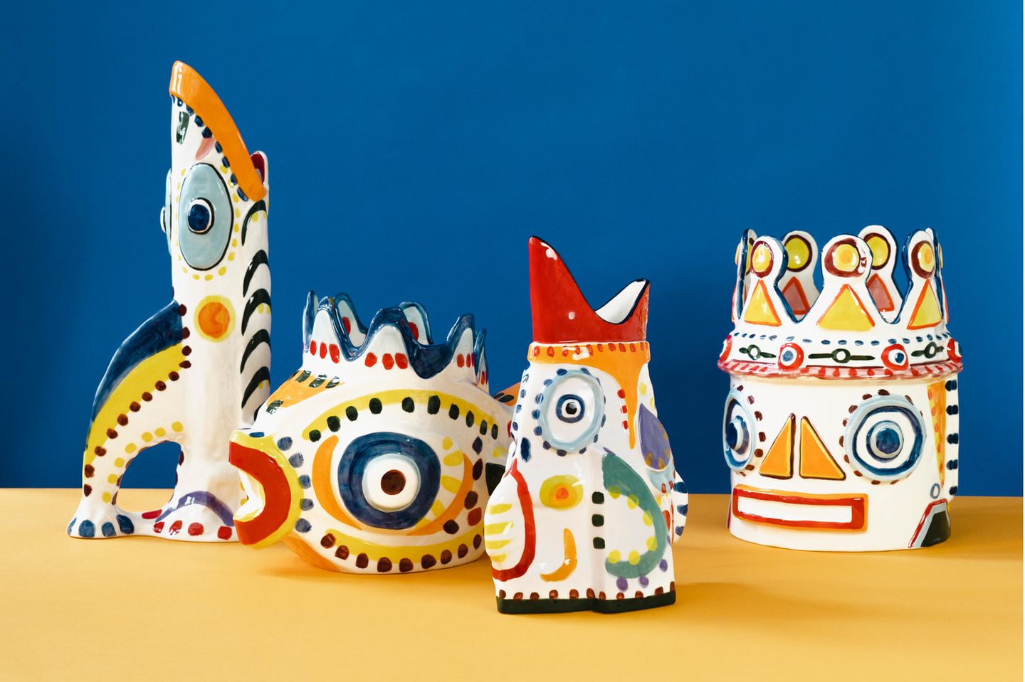 Vier abstrakte Vasen in Form von Köpfen und Fischen stehen auf blau-gelben Grund