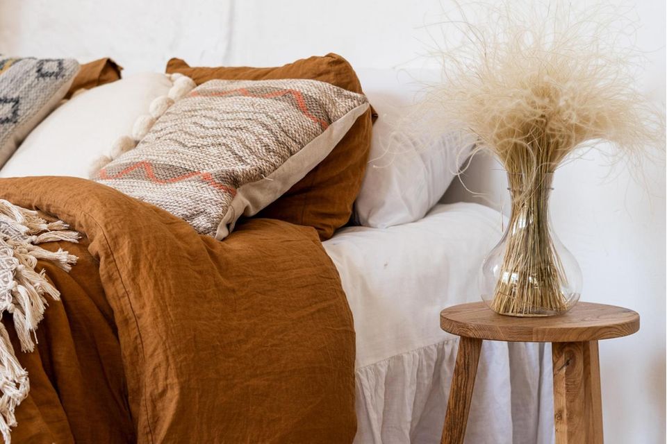 Bett mit weißem Laken an weißer Wand mit erdfarbener Bettwäsche & Ethno-Kissen Boho