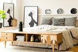 Schlafzimmer mit schwarz-weiß gemusterten Kissen, Wandtellern und Bildern hinter einem Sideboard aus Holz
