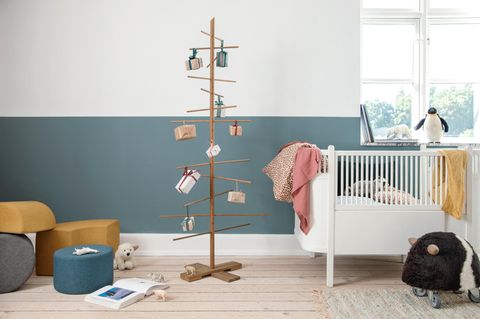 Aus Eiche gefertigter, wiederverwendbarer Weihnachtsbaum mit eingepackten Geschenken neben einem Kinderbett