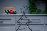 Mit Lichterkette und Weihnachtskugeln dekorierter Baum aus Metall vor einer grauen Vintage-Kommode