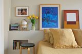 Schlafzimmer mit Bettwäsche in Senfgelb, kleinen Nischen für Bücher und Podest mit Kunst