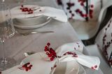 Gedecks einer Weihnachtstafel mit weißem Geschirr, dezenter Tischdecke und weißen Stoffservietten mit Stechpalme
