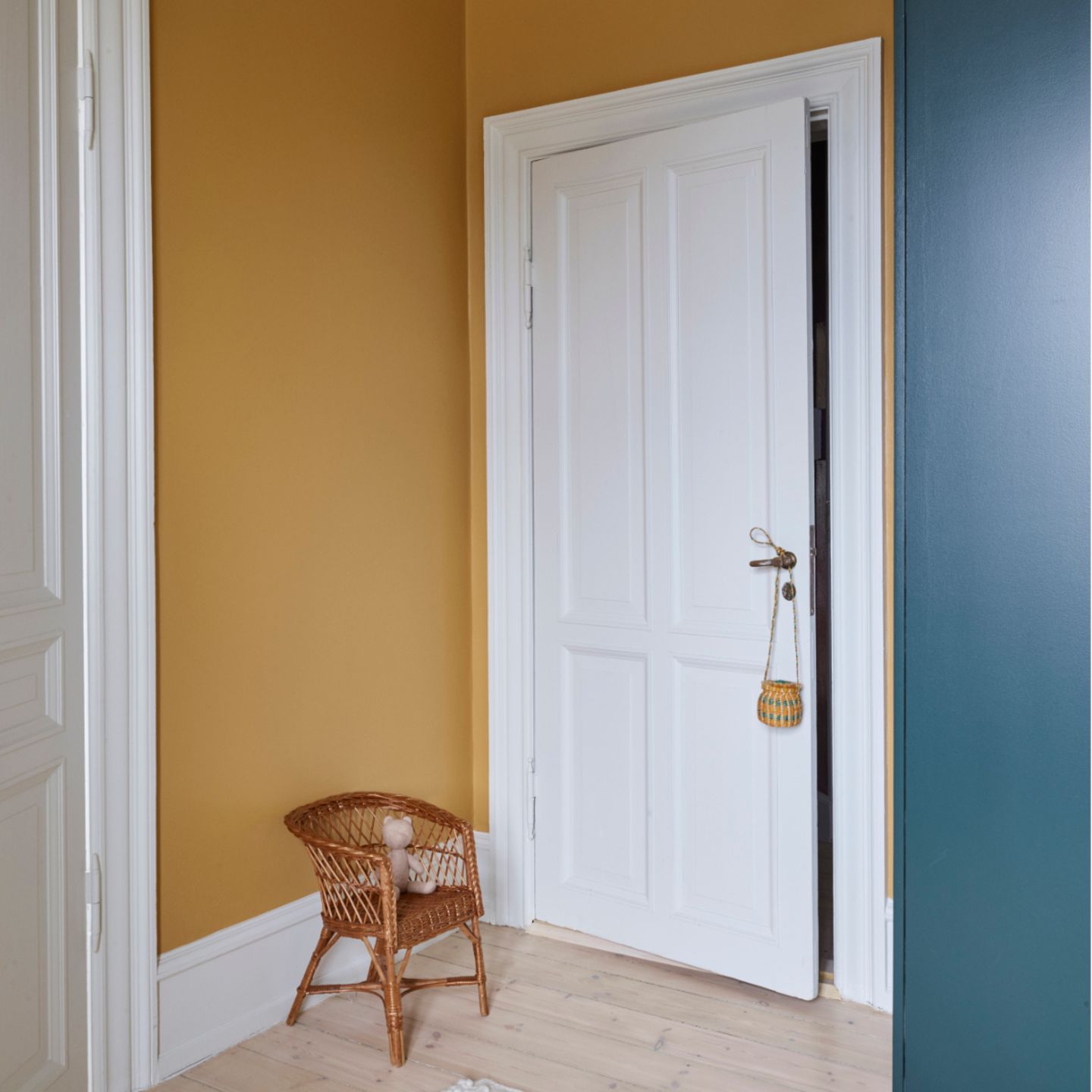 Weiß lackierte Tür mit passendem Türrahmen an gelber Wand mit Korbstuhl