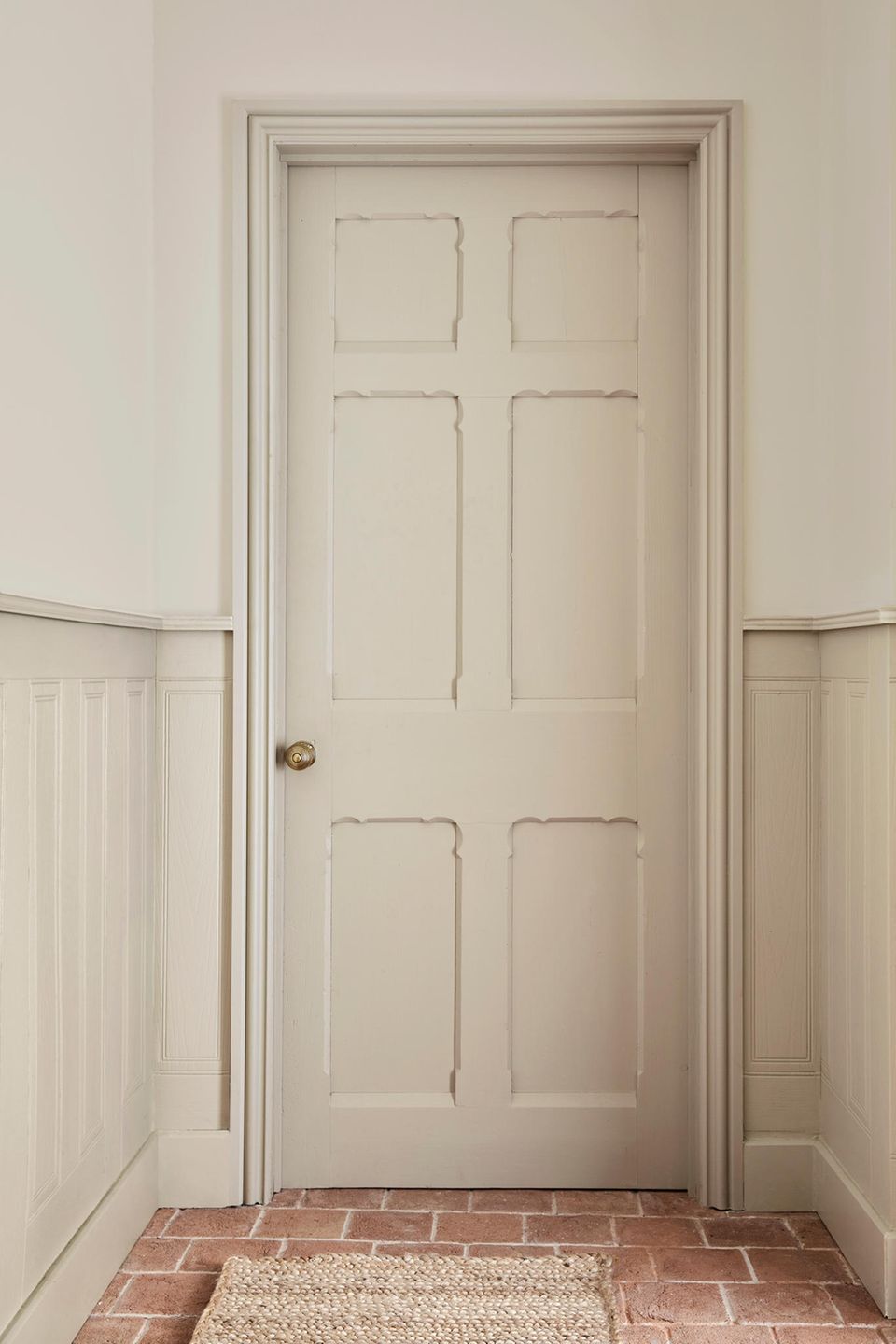 Tür und Türrahmen in hellem Beige mit Deko-Kassetten am Ende eines weißen Flures