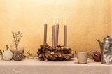 Ein Adventskranz aus Zapfen, getrockneten Gräsern sowie vier Stabkerzen stehen auf einem Tisch mit einer Vasen und Kugeln