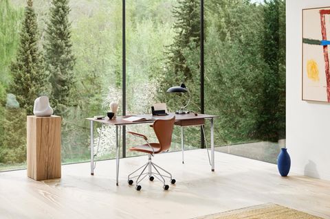 Ein Schreibtisch mit Holtplatte und Chromebeinen steht mit einem Lederstuhl vor einer großen, grünen Glasfront