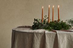 Adventskranz auf einer Leinentischdecke vor einer beigen Wand mit gedrehten Kerzen.