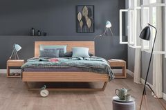Holzbett mit grüner Bettwäsche steht vor einer grauen Wand