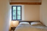 Schlafzimmer in einem Altbau mit offenen Balken und Sprossenfenster
