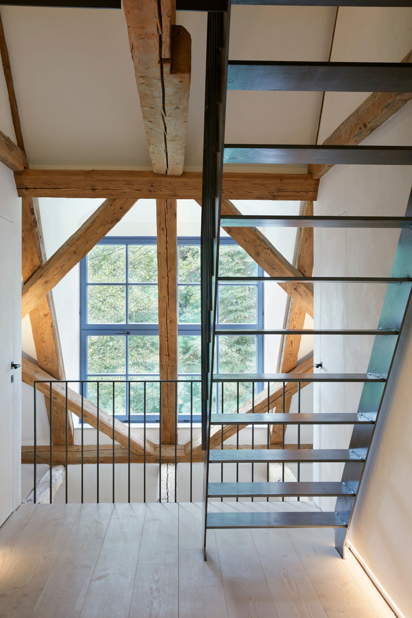 Stahltreppe vor offenen Holzbalken mit Blick auf ein blaues Sprossenfenster