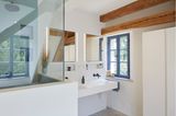 Badezimmer in einem Altbau mit offenen Balken und einer Glasabtrennung für die Dusche