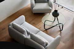 Hellgraues kleines Sofa mit Sessel in derselben Farbe kombiniert zu einem Glastisch auf Holzboden