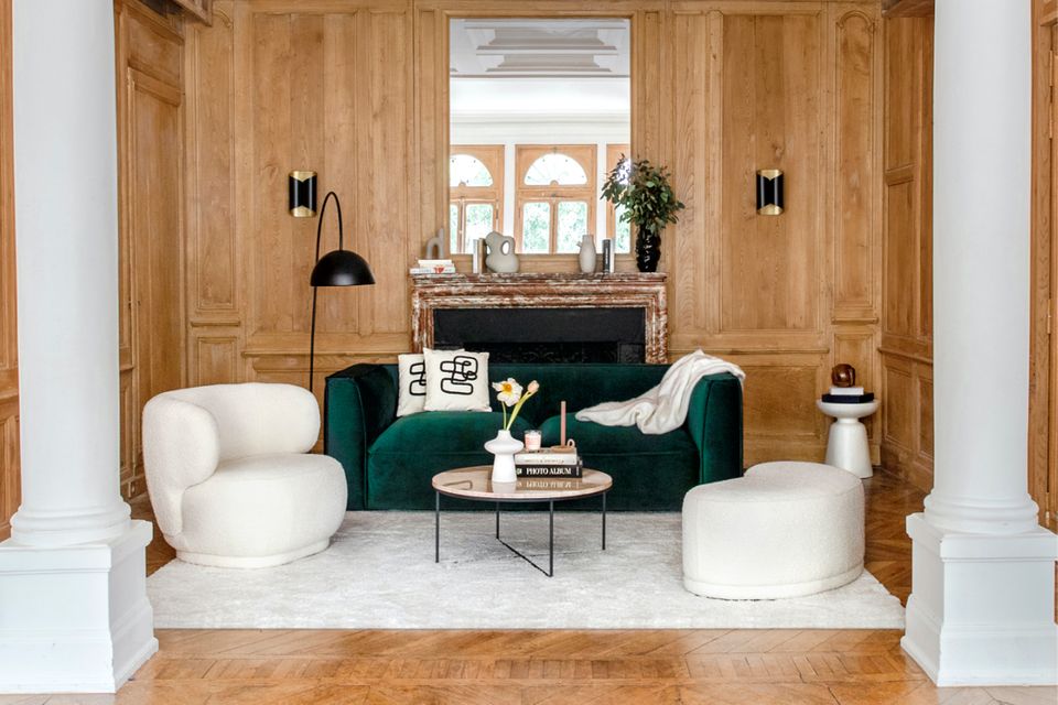 Sofa aus grünem Samt mit weißem Sessel, weißem Hocker vor heller Wandverkleidung