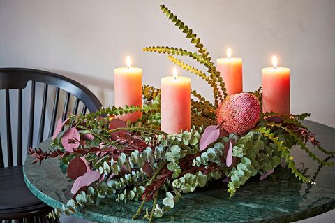 Adventskranz mit lachsfarbenen Kerzen, Proteablüten und Eukalyptus auf einem schwarzen Tisch.