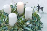 Adventskranz mit Eukalyptuszweigen und weißen Stumpenkerzen auf einem weißen Holztisch