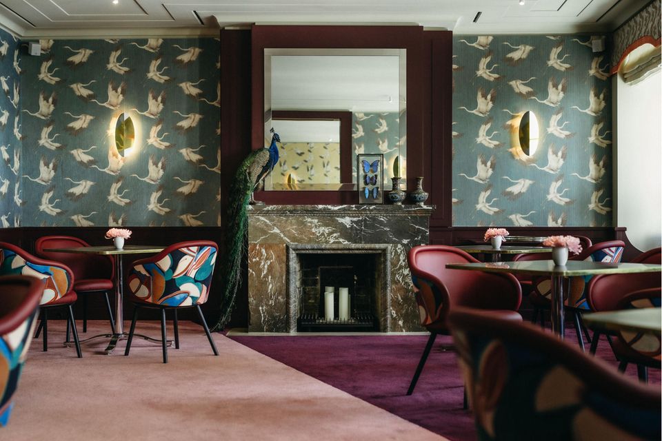 Gastraum des Restaurant Alois in München mit Kranichtapete in Petrol, rosafarbenem Teppichboden und bunten Stühlen